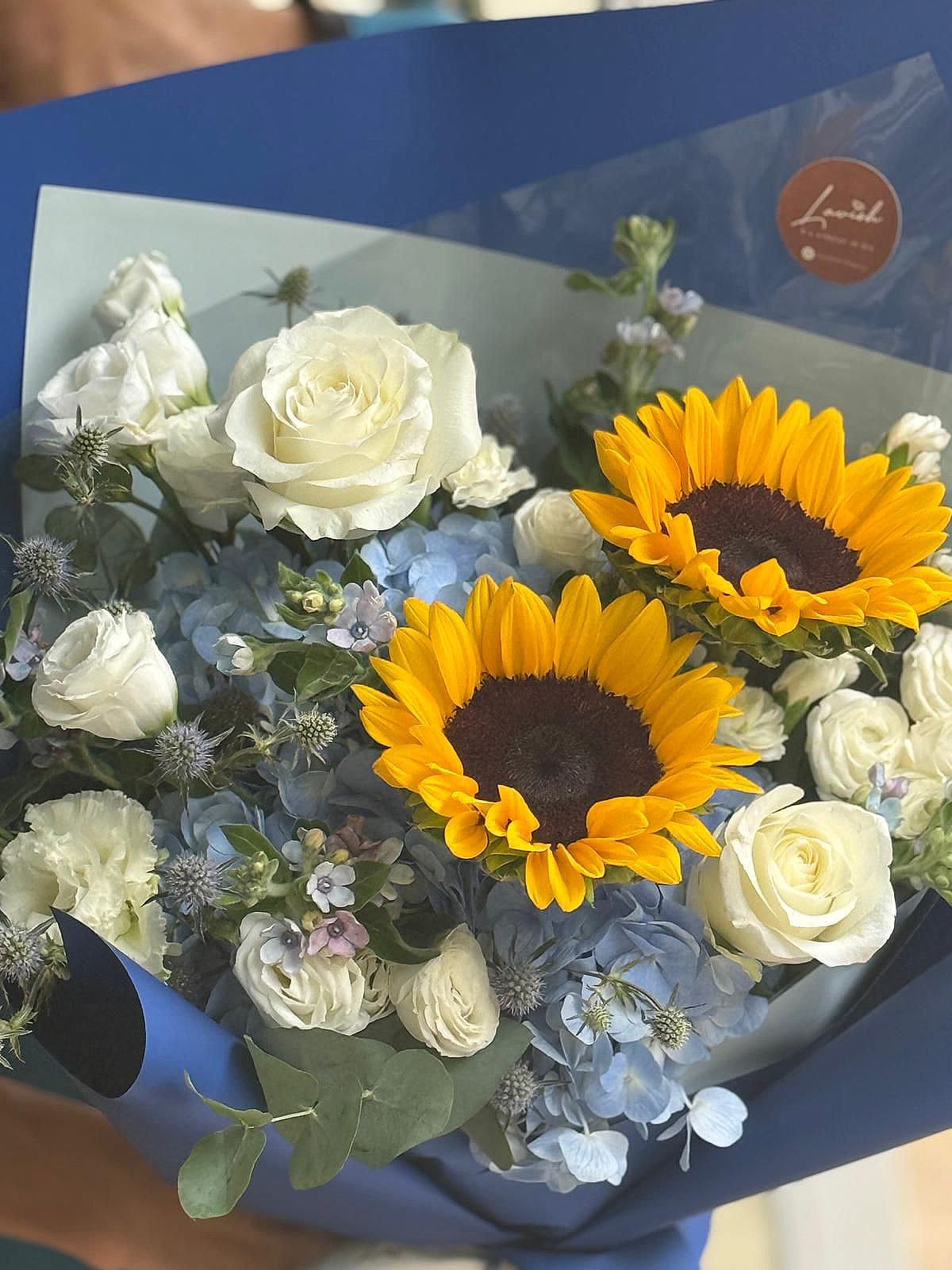 Bouquet of flowers with sunflowers and white roses in a blue wrap.