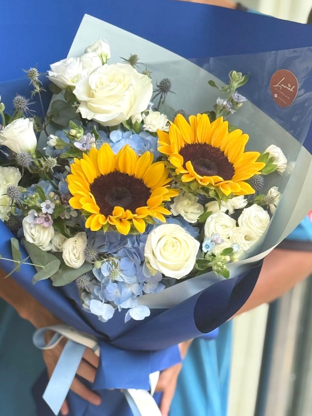 Bouquet of flowers with sunflowers and white roses in blue paper wrap.