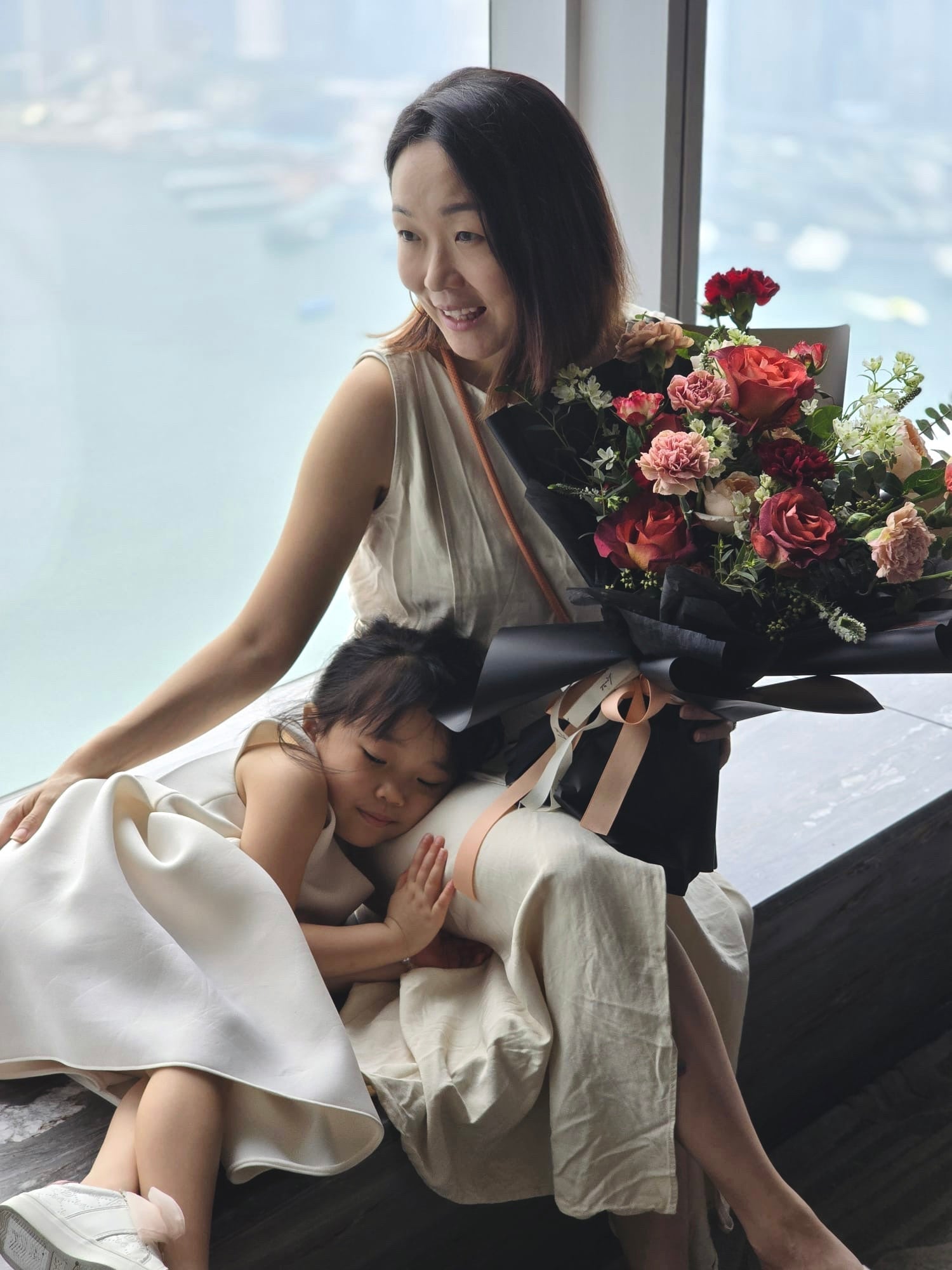 Mother's Day flower bouquet collection: The founder of Lavish Florist holding a premium red and pink Mother's Day bouquet while sharing a warm, tender moment with her daughter by the window.