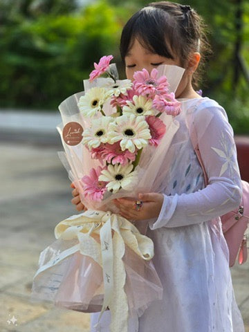 由Lavish Florist設計的Pink Gerbera Dream幼稚園畢業花束細節展示，小女孩低頭輕抱粉色與奶油白雙色非洲菊（太陽菊）花束，搭配夢幻透光包裝紙與 Lavish 專屬絲帶。